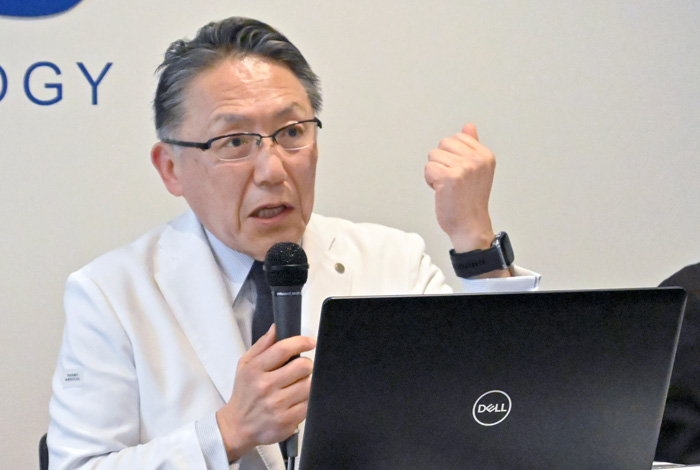腕のスマートウオッチを示して説明する神野理事長